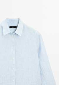 Camicia azzurro chiaro a maniche lunghe con bottoni, realizzata in un tessuto testurizzato con sottili righe verticali, dotata di un colletto classico e bottoni bianchi.