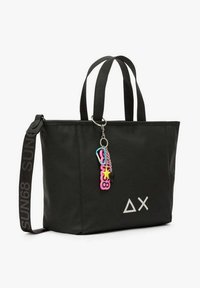 Sort tote-taske med to håndtag, en aftagelig nøglering og et geometrisk logo på forsiden. Fremstillet af slidstærkt materiale med et struktureret design.