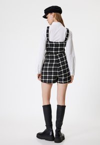 Vestido mini a cuadros en blanco y negro con tirantes gruesos, combinado con una camisa blanca de botones y botas de cuero negras hasta la rodilla.