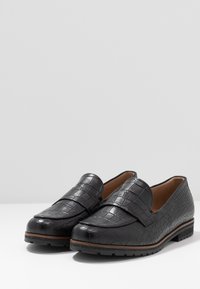 Mocassins en cuir noir avec un motif texturé semblable à du crocodile. Bout arrondi, col rembourré et semelle extérieure texturée basse ajoutent un détail fonctionnel.