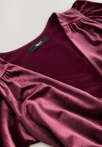 Burgunderfarbene Satinbluse mit weicher Textur, gerafften Ärmeln und Rundhalsausschnitt, ausgestattet mit einem schwarzen Etikett mit dem Aufdruck "NEXT".