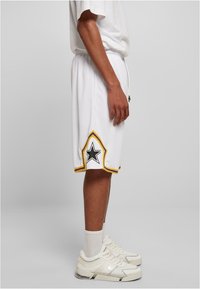 Baltas sporta šorts ar elastīgu jostu, ar zvaigžņu grafiku melnā krāsā un dzelteniem un purpursarkaniem akcentiem. Valkāti ar baltām čības un zeķēm.