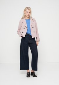 Ροζ διπλόστενη ζακέτα, μπλε πουλόβερ και σκούρα τζιν με φαρδύ πόδι. Το ντύσιμο ολοκληρώνεται με μαύρα παπούτσια με τακούνι. Απλός, μοντέρνος σχεδιασμός.