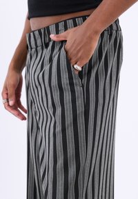 Pantaloni drepți cu dungi negre și gri, având două buzunare laterale și o textură de stofă netedă. Accentuati cu o verigă la mână.