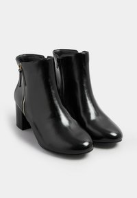 Par de botines de cuero negro con tacones de bloque y cremalleras doradas laterales sobre un fondo blanco.