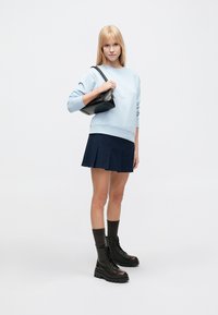 Ανοιχτό μπλε φούτερ με ριμπ μανσέτες, σκούρο μπλε πλισέ φούστα, μαύρα μποτάκια μέχρι τον αστράγαλο και μια μικρή μαύρη τσάντα ώμου. Λείες υφές και αντιθετικά χρώματα.