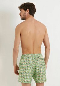 Shorts de baie verzi cu un design cu personaje de desen animate, talie elastică și croială lejeră, văzute din spate.
