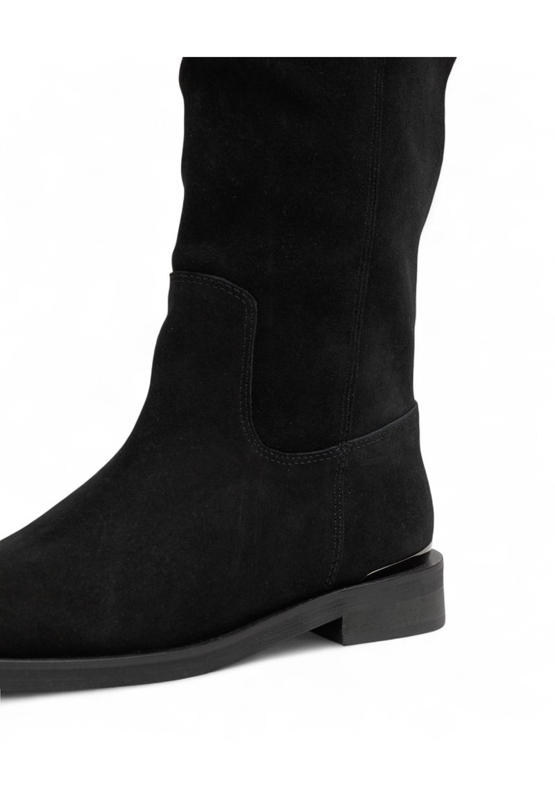Stivale nero in suede alta fino al ginocchio con un taglio laterale rettangolare, texture liscia e tacco basso a blocco. Dettagli di cucitura minimi.