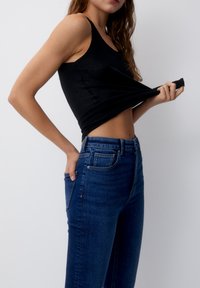 Débardeur noir ajusté associé à un jean en denim bleu foncé taille haute. Le débardeur a des bretelles fines ; le jean possède des poches avant et une finition lisse.