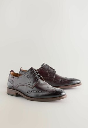 Braune Leder-Dressschuhe mit Flügelspitze, dekorativen Perforationen und glatter Oberfläche; mit Schnürsenkeln und niedrigem, gestapeltem Absatz.