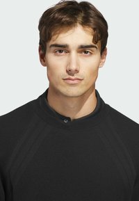 Black pullover with a textured fabric, round neck, and button detail. Features raglan sleeves with subtle stitching accents.