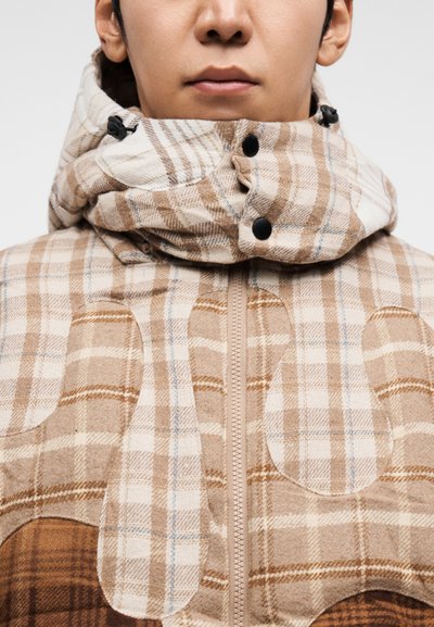 Μπεζ καρό μπουφάν με ψηλό γιακά, που διαθέτει φερμουάρ και μαύρα κουμπιά τύπου κλικ, κατασκευασμένο από μαλακό ύφασμα με υφή και διακοσμ ητικές χαραγμένες λεπτομέρειες.