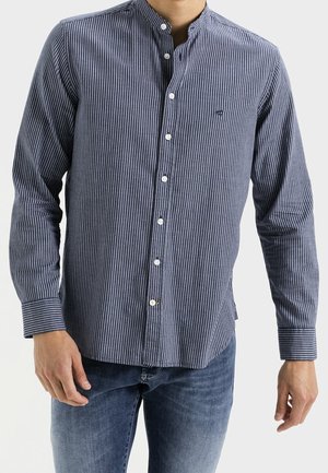 Homme portant une chemise à rayures verticales bleu marine et blanches avec col mandarin et jean bleu.