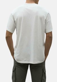 Camiseta blanca de algodón con cuello redondo y mangas cortas, que presenta un diseño liso y un ajuste relajado. Se muestra la vista trasera, sin gráficos visibles.