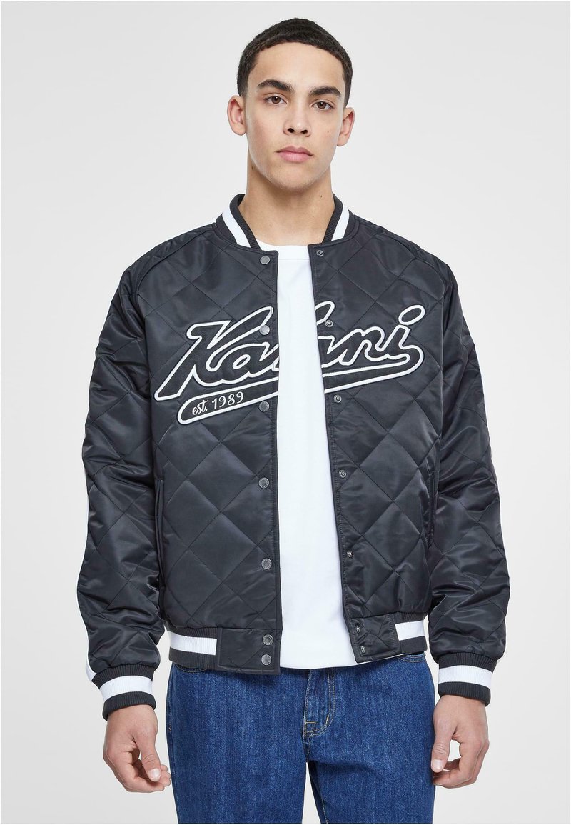 Black quilted bomber jacket with white accents, featuring a logo on the chest, snap front closure, and striped ribbed cuffs and hem.
