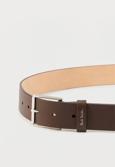 Pruun nahkvöö, sileda viimistlusega, hõbedane metallrihm ja logomärgiga silt. Varustatud mitme auguga, mis võimaldavad suurust reguleerida.