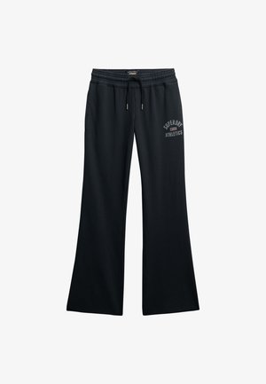 Pantalon de survêtement large noir avec taille élastique, cordon de serrage, poches latérales et logo "Superdry Athletics" sur la cuisse gauche.