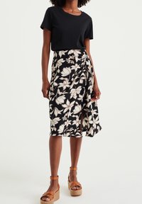 Černá květinová sukně s bílými a béžovými květy, kombinovaná s černým tričkem. Má asymetrický lem a hnědé platformové sandály.