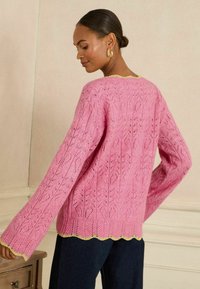 Roze gebreide trui met een kantpatroon, afgezet met een golvende zoom met gouden bies, lange mouwen en een losse pasvorm.