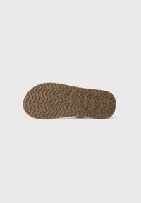 Semelle de chaussure en caoutchouc brun avec un motif de bande de roulement en zigzag, surface texturée et forme arrondie. Pas de marquage ou de détails supplémentaires visibles.
