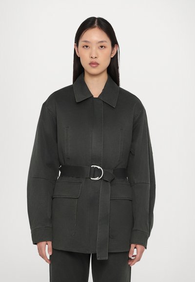 Giacca nera con cintura in vita, realizzata in cotone, con colletto, ampie tasche frontali e vestibilità rilassata. Texture liscia e design minimale.
