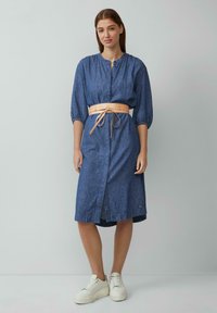 Jeans-Midi-Kleid in Blau mit durchgehendem Knopfverschluss, dreiviertel Ärmeln und einem beigen Gürtel. Kombiniert mit weißen Plateausneakern.