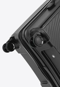Valise rigide noire avec surface texturée, zips et doubles roues. Elle est dotée de protections d'angle robustes et de poignées renforcées.