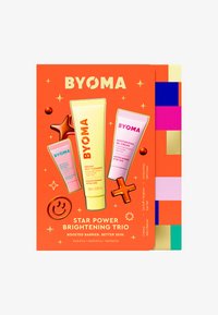 BYOMA Star Power Brightening Trio Box, orange Hintergrund, enthält drei Tuben: gelbes, cremiges Jelly-Reinigungsprodukt, rosa feuchtigkeitsspendende Gel-Creme und blaues Augen-Gel mit bunten Akzenten.