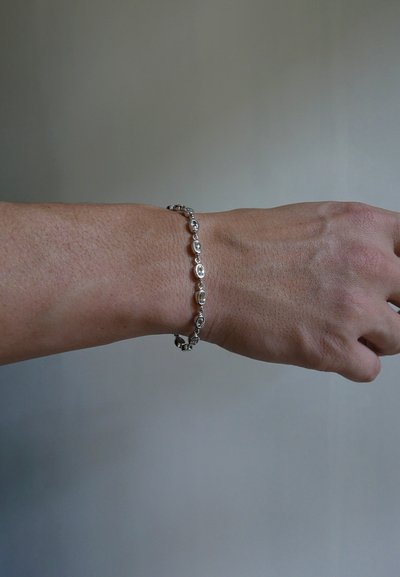 Silver bracelet on wrist featuring oval links with alternating circular accents. Smooth texture against tanned skin, simple design.