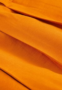 Oranžová látka vykazuje hladkou texturu s záhyby. Materiál se zdá být lehký a v některých oblastech má mírný lesk.
