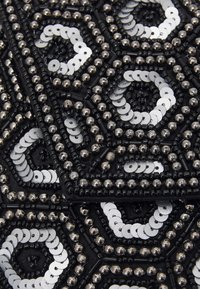 Černá látka zdobená hexagonálními vzory z černých korálků a stříbrných flitrů, s různými texturami a kontrastními povrchy.