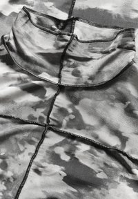 Primo piano di un tessuto tie-dye nero e grigio con cuciture overlock visibili e un dettaglio del colletto piegato.