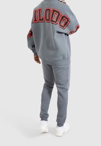 Sudadera gris con la palabra "HILODO" en letras rojas en la espalda, combinada con pantalones deportivos grises a juego y zapatillas blancas, mostrada desde atrás.