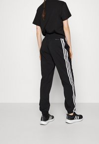 Czarne sportowe spodnie z białymi paskami po bokach, elastycznym pasem i zwężanymi mankietami, zestawione z czarnymi tenisówkami z białymi akcentami.