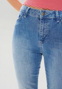 Gai zilu džinsu bikses ar šauru piegriezumu, kas piedāvā tradicionālo piecu kabatu dizainu, mazu metāla pogu un smalku faktūru.