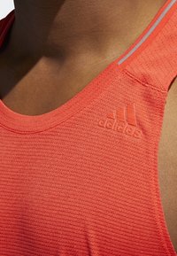 Rotes sportliches Tanktop mit strukturiertem Muster, Rundhalsausschnitt und grauen Akzentstreifen. Enthält ein geprägtes Adidas-Logo.