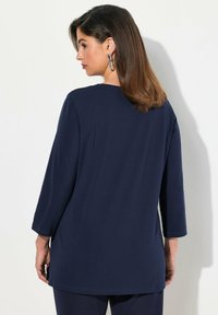 Marineblaues Langarmoberteil aus weichem Stoff, mit Rundhalsausschnitt und einem etwas längeren Rücken sowie seitlichen Schlitzen für mehr Bewegungsfreiheit.