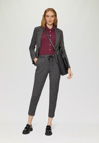 Blazer gris ajusté sur une chemise bordeaux, associé à un pantalon gris ajusté. Les chaussures sont des mocassins noirs, accompagnés d'un sac à bandoulière noir.