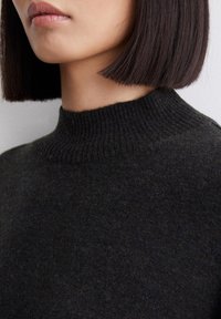 Pull en laine foncée avec un col montant côtelé et une finition douce et texturée. Le tissu semble confortable et chaud, affichant une couleur profonde et atténuée.