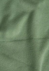 Close-up van zacht, groen ribgebreid materiaal met lichte kreukels en zichtbare textuur in natuurlijk licht.