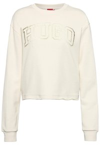 Sudadera de color crema con un diseño recortado, que presenta letras texturizadas de "HUGO" y un acabado de tela suave. Mangas largas y puños acanalados.