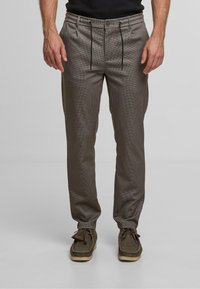 Strukturerede, brune ternede bukser med en snoretræk i taljen og to frontlommer, parret med mørkegrønne sko.