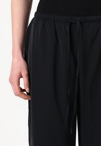 Sorte, lette, stretchy bukser med elastisk linning og snor. Har en glatt tekstur og sidelommer.