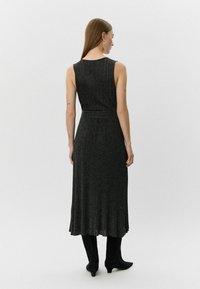 Zwarte, geribbelde, mouwloze jurk met een getailleerde taille en een uitlopende zoom, in combinatie met kniehoge zwarte laarzen. Gladde textuur met subtiele glans.