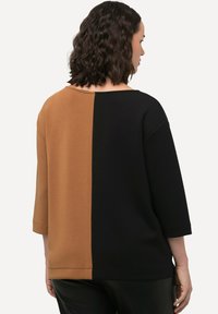 Pestrý oversized top s blokováním barev, který má jednu hnědou a jednu černou stranu. Je vyroben z měkkého materiálu, s rukávy po tři čtvrtiny a širokým výstřihem.
