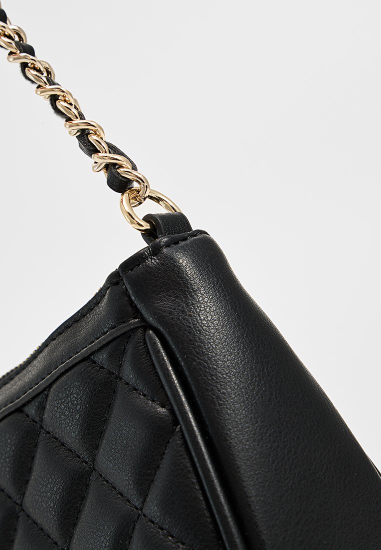 Borsa a tracolla nera trapuntata con una texture in pelle liscia. Presenta una tracolla in catena dorata e un design affusolato. La vista laterale mostra una cucitura dettagliata.