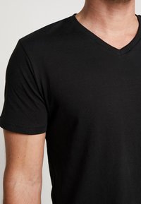 T-shirt noir à manches courtes en V, fabriqué en coton doux. Présente une coupe ajustée et une texture lisse avec un minimum de détails de couture.