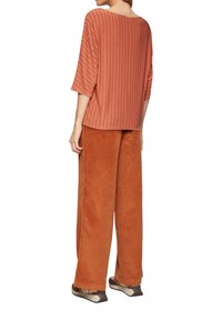 Rust gestreepte blouse met driekwartmouwen, gecombineerd met brede rust kleurige corduroy broek. Het schoeisel heeft een neutrale kleurencombinatie.