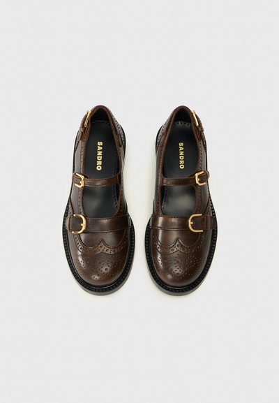 Bruine leren schoenen met twee gespen, geprononceerde randen en brogue-details, met een ronde neus en een gestructureerde zool.