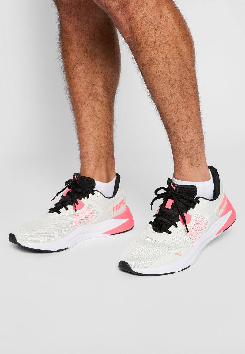 Hvite treningssko med svarte detaljer og knallrosa innslag. Overdel i mesh, rund tå og snøring. Med Puma-logo.